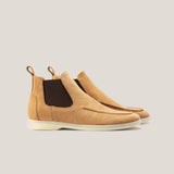 A pair of light beige suede Chelsea boots with a white sole and dark brown detailing.