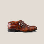 A single monkstrap shoe in light cognac brown, hand patinated on crocodile patterned leather with a square buckle.