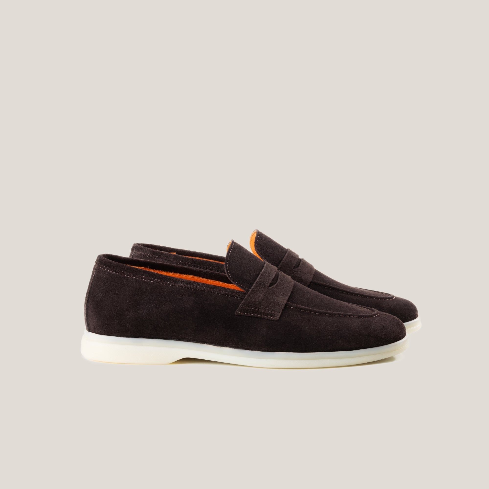 A pair of dark brown suede penny loafers with a white sole.